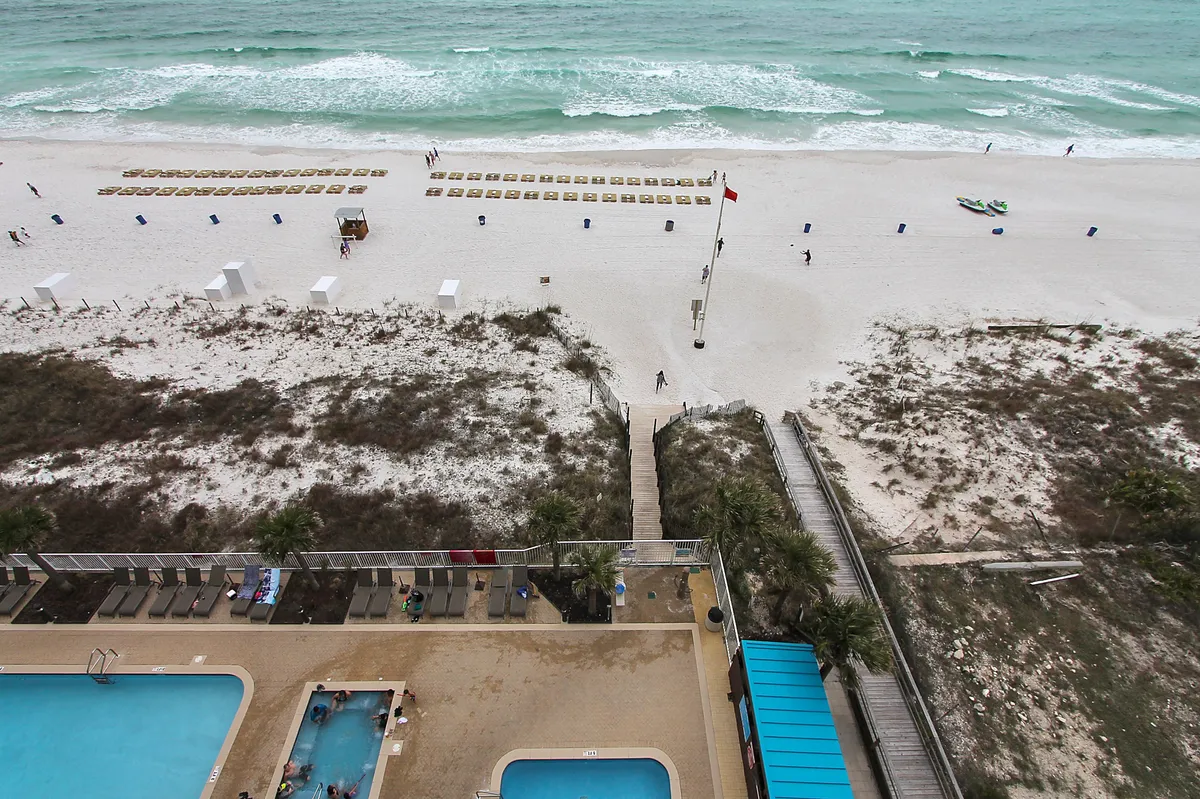 This image captures a stunning beachfront scene with swimming pools, a boardwalk, beach chairs, and gentle ocean waves in the background. The atmosphere is relaxed and inviting, suggesting both leisure and romance by the water.