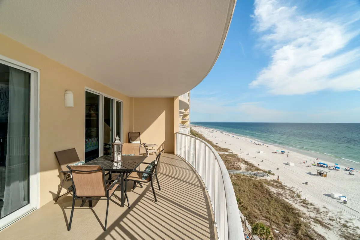 An inviting balcony scene overlooking the beach features comfortable seating and panoramic ocean views. The golden sunlight illuminates the sand and water, offering a tranquil vantage point to watch for dolphins, enjoy meals, or simply relax above the waves.