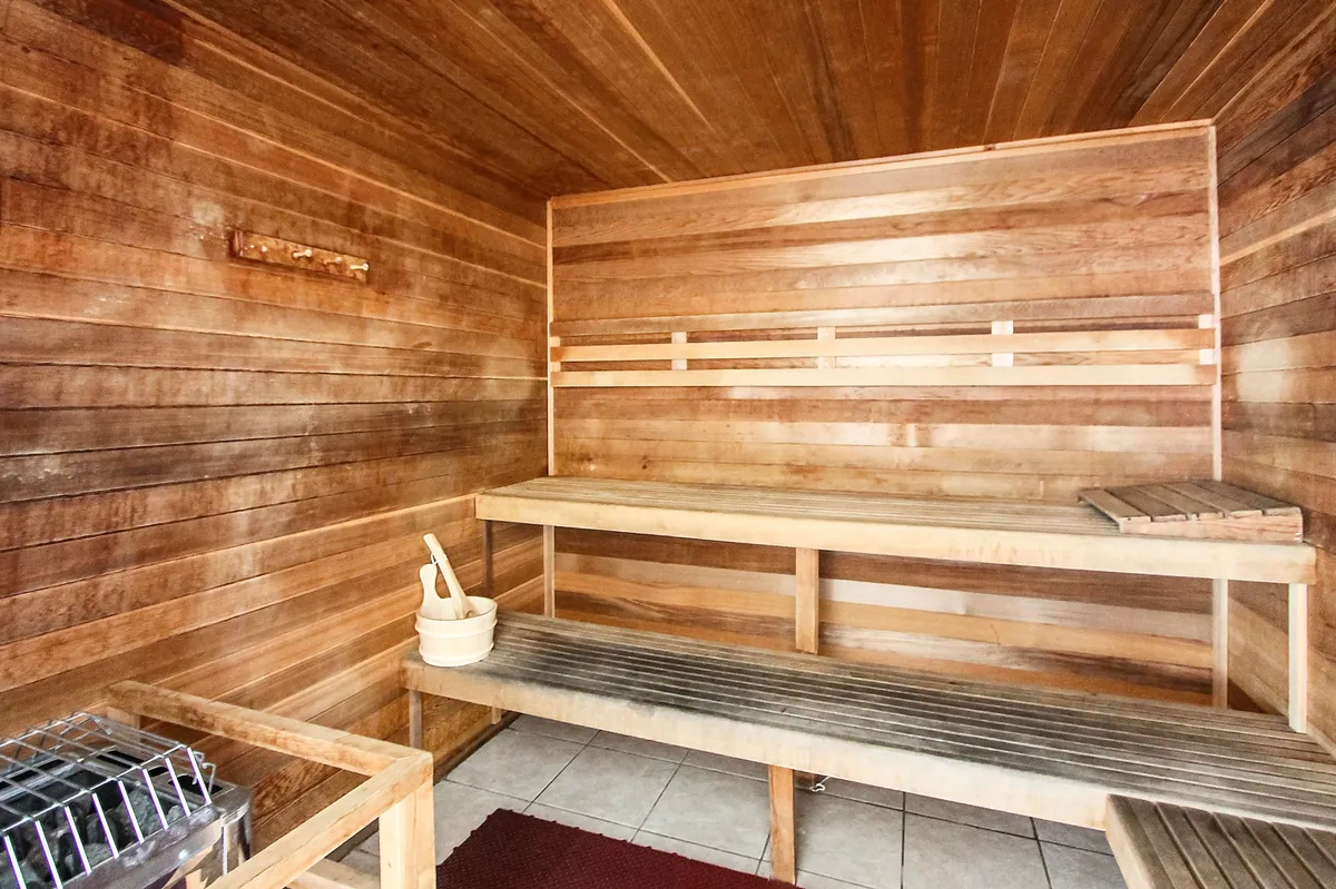 This interior image shows a serene sauna with wooden benches, a basket for sauna accessories, and a stone heater. The calming atmosphere hints at relaxation and wellness experiences shared by couples.