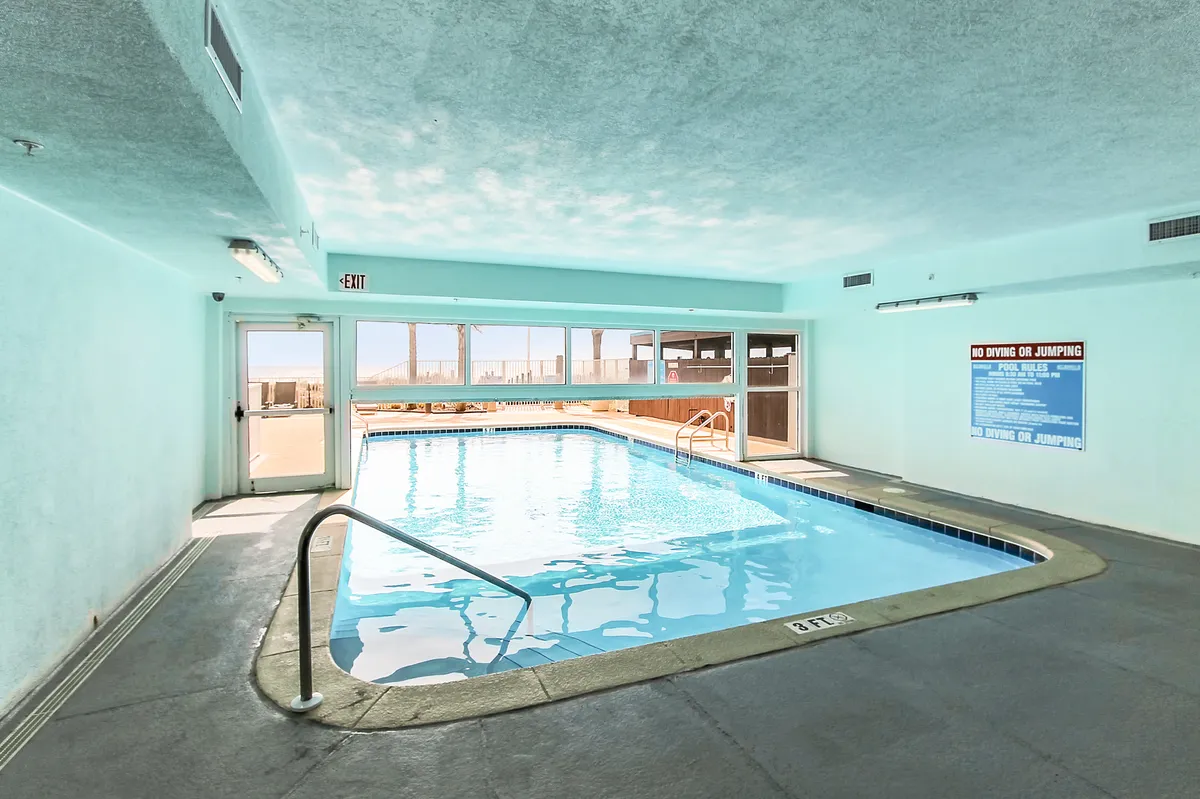 A bright and inviting indoor swimming pool area, featuring large windows that let in natural light. The pool is surrounded by sleek railings and ample space for lounging, creating a rejuvenating atmosphere for swimming or relaxing indoors, regardless of the weather.