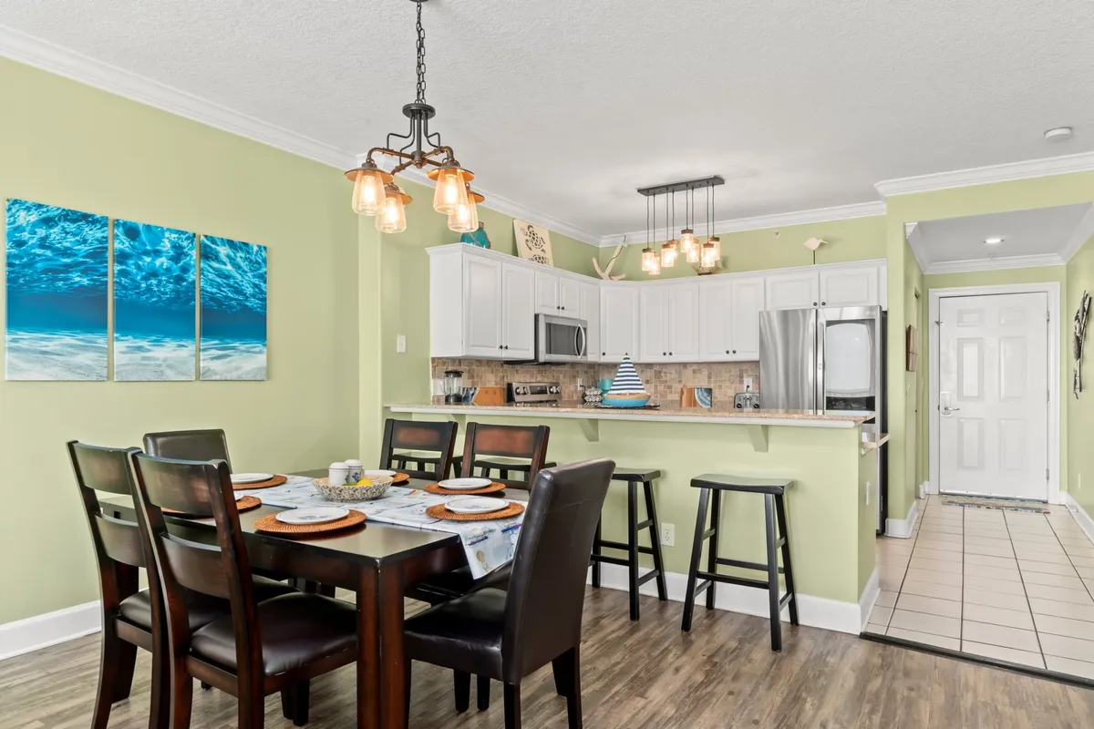 The image presents a dining area adjacent to a kitchen island, with a family-style dining table and modern artwork on the walls. The setting is welcoming, designed for shared meals and memorable gatherings.