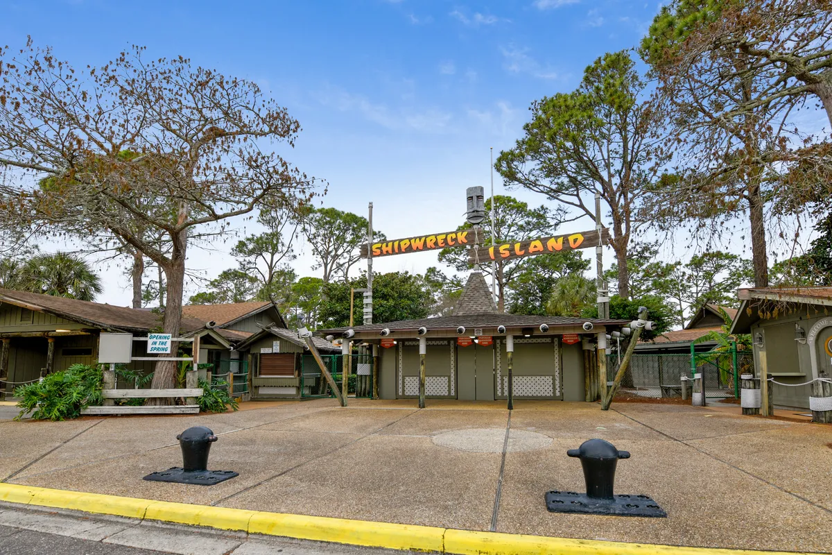 The entrance to Shipwreck Island Water Park is marked by a bold, playful sign surrounded by lush landscaping and trees. The inviting atmosphere promises fun-filled family outings and excitement just a short trip from the condo.