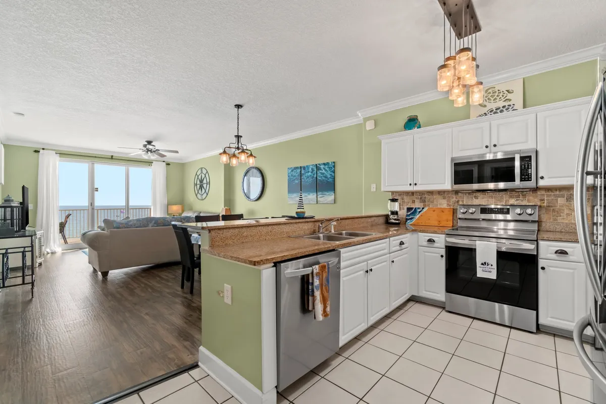 This interior image features an open-concept space with a modern kitchen equipped with stainless steel appliances, a dining table under stylish pendant lighting, and a living room area facing a large balcony with an ocean view. The overall design is upscale yet welcoming, with plenty of natural light and a seamless flow between the kitchen, dining, and living spaces.